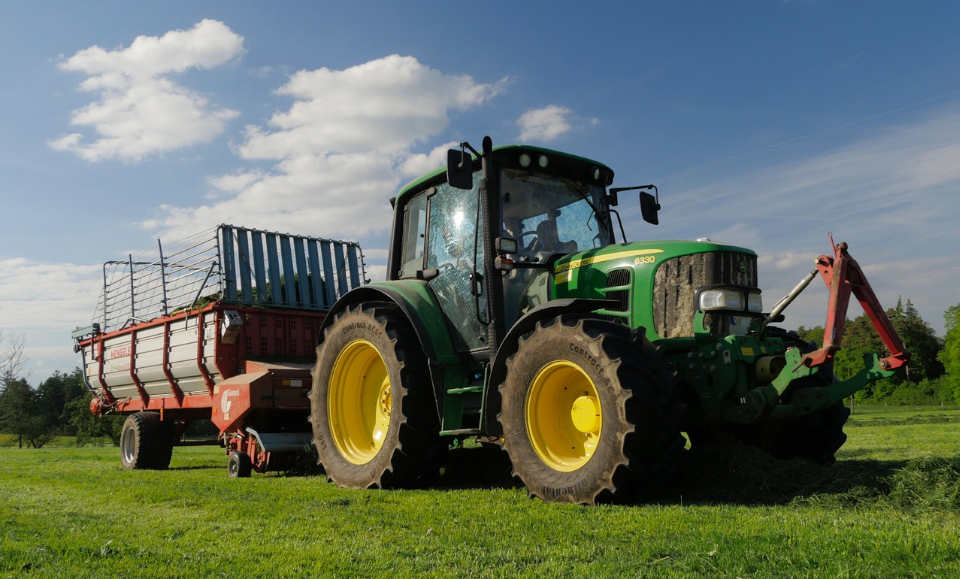 John Deere 6330 steht mit Anhänger auf einer Wiese